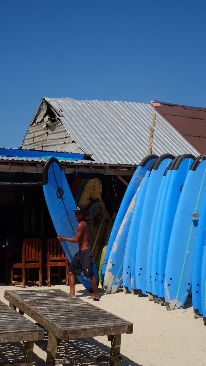 Instructor carrying a surfboard past the board racks
