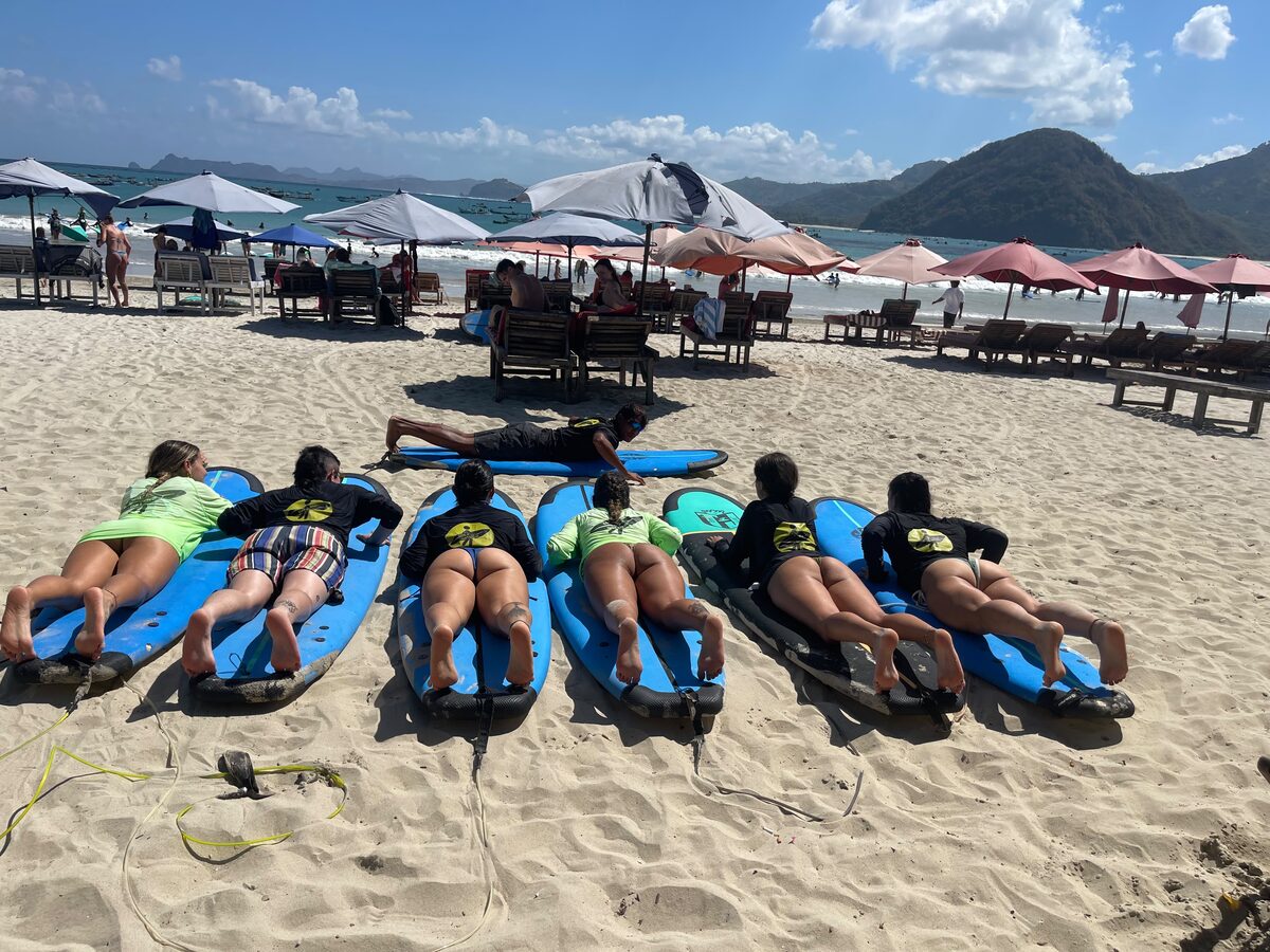 Group stretching on surfboards with the beach and umbrellas behind