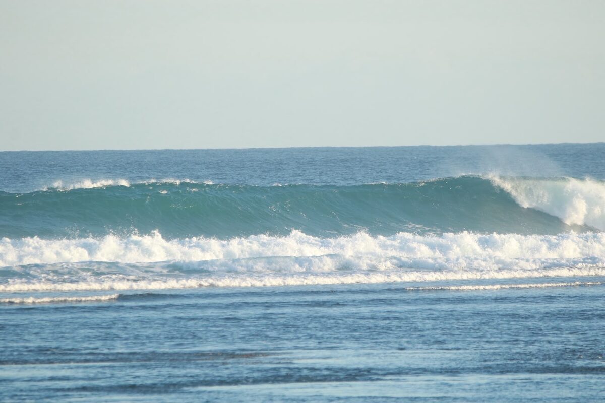 Surfers paddling under a breaking wave in Lombok