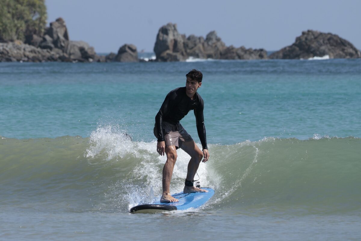Student surfing a wave with a rocky headland behind